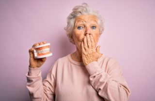 woman holding dentures in one hand and the other is across her mouth dentures missing teeth Cohoes New York