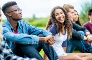 girl laughs while looking at the camera. She is sitting outside on the grass, in a row of teens vaping tooth decay dentist in Cohoes New York
