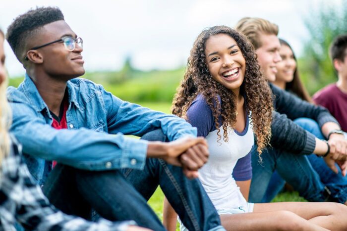 girl laughs while looking at the camera. She is sitting outside on the grass, in a row of teens vaping tooth decay dentist in Cohoes New York